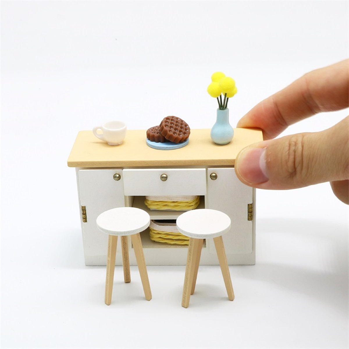 Miniature countertop and stools being placed by a comparatively large hand.